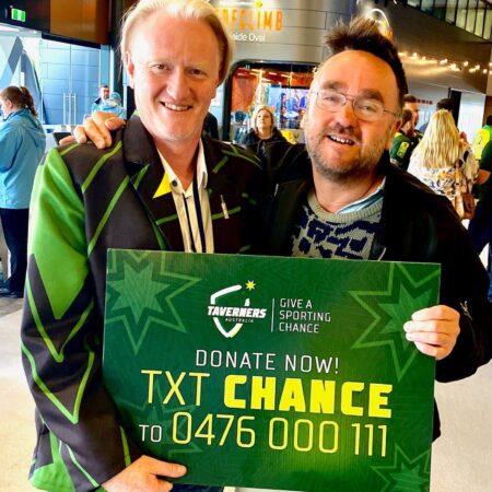 Managing Director Sunny and a spectator both proudly holding up the Donate Now, Text to Donate sign in the lobby of the Adelaide oval.
