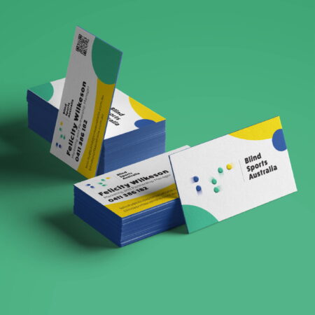 A stack of the new BSA business cards, showing the front, which is mainly white, with the new BSA logo in the middle, and big graphic overlapping circles, on the corners of the card, in the same colours as the logo. You can also see the back of the cards, with an example of the persons details, which are written in english and also embossed braille. There is also a small QR code on the back, which takes the user directly to the BSA website.